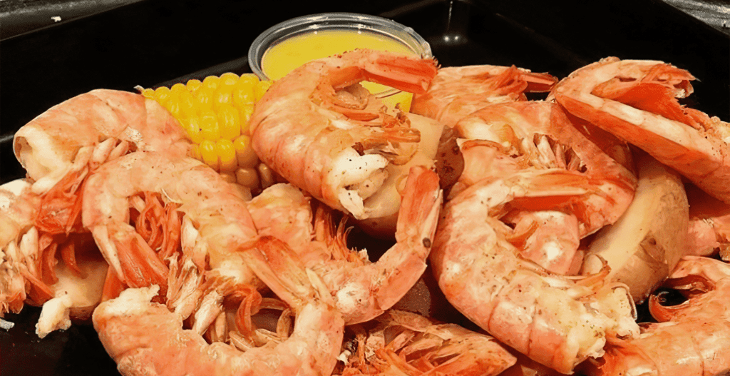 A plate of cooked shrimp and corn on the cob.